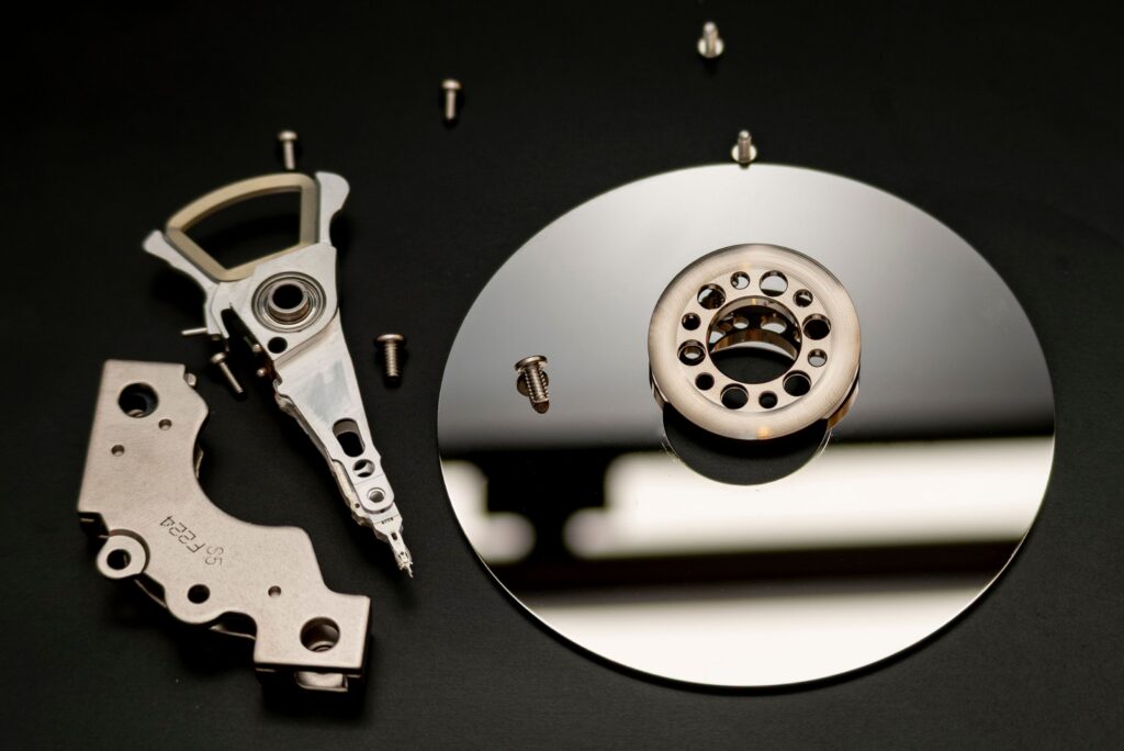 Close-up of dismantled hard drive parts with a reflection on a black surface, showcasing intricate mechanical details.