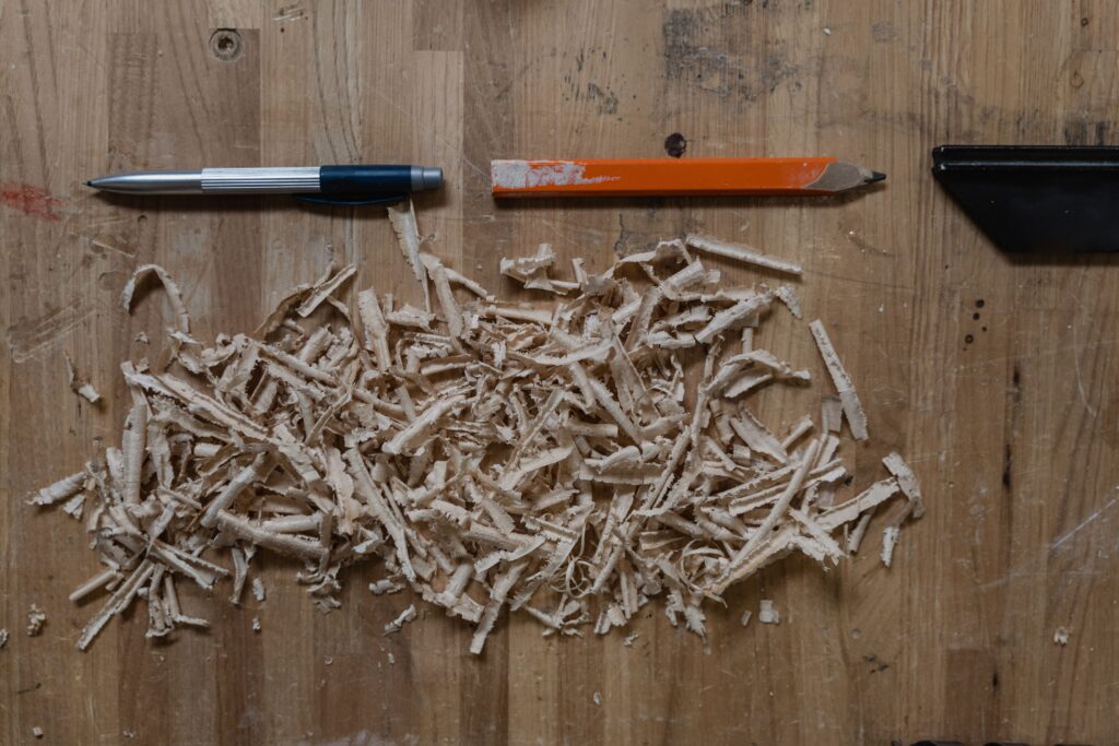 Close-up of wood shavings with a pen and a pencil on a wooden workbench, depicting craftsmanship.