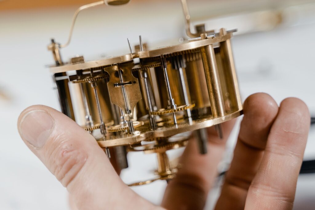 Close-up of a vintage clock mechanism held by hands, showcasing intricate details.